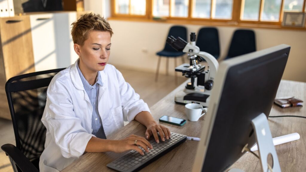 A woman in a lab coat typing on a computer.