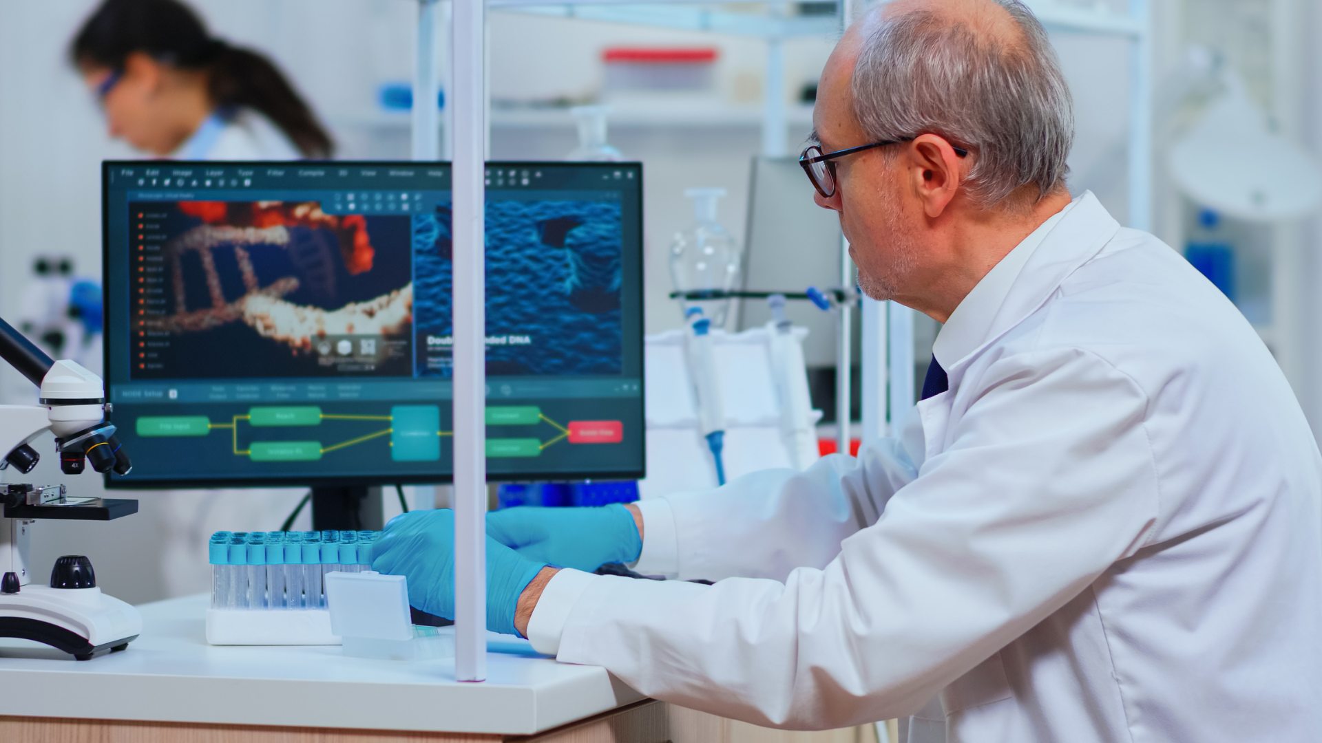 Scientist in a lab coat uses a computer displaying DNA analysis, with test tubes and a microscope nearby.