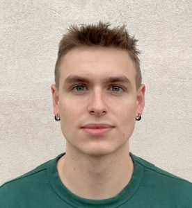 A member of Delta4's team, with short hair and hoop earrings, stands confidently against a plain light-colored background in a green shirt.