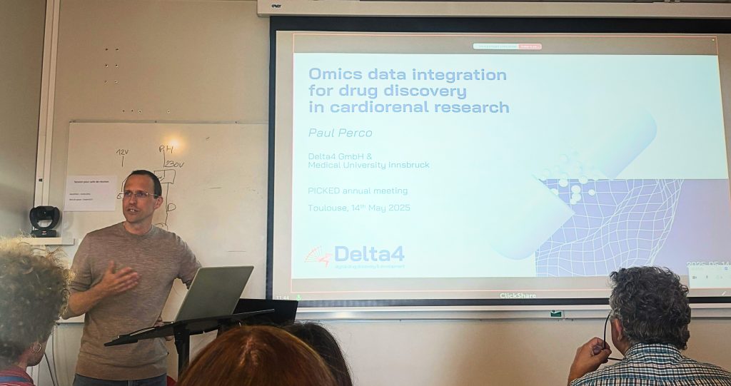 A picked presenter stands beside a screen displaying a presentation titled "Omics data integration for drug discovery in cardiorenal research" at the Delta4 PIC4Card annual meeting in Toulouse, May 2025.