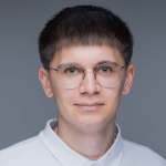 A young man with short dark hair and round glasses, part of Delta4's team, wears a white collared shirt and faces forward against a plain gray background.