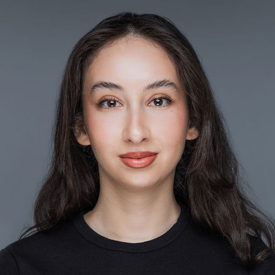 A woman with long dark hair, wearing a black top, faces the camera with a neutral expression against a gray background, representing Delta4's team.