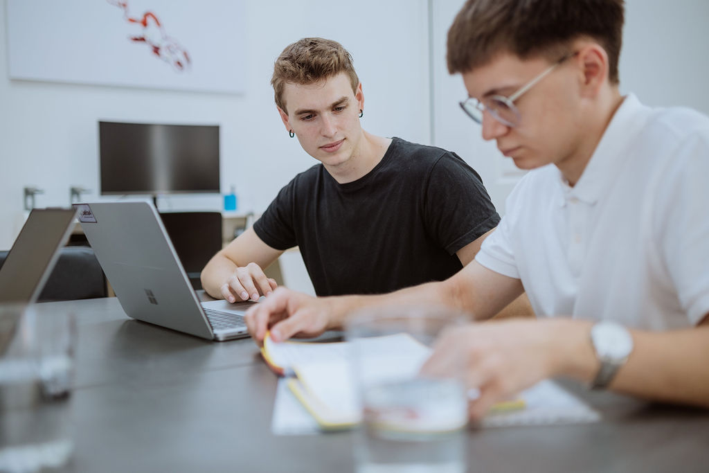 Two people sit at a table with laptops and notebooks, focused on their work in a bright, modern office setting as they collaborate on new advances in personalized medicine.