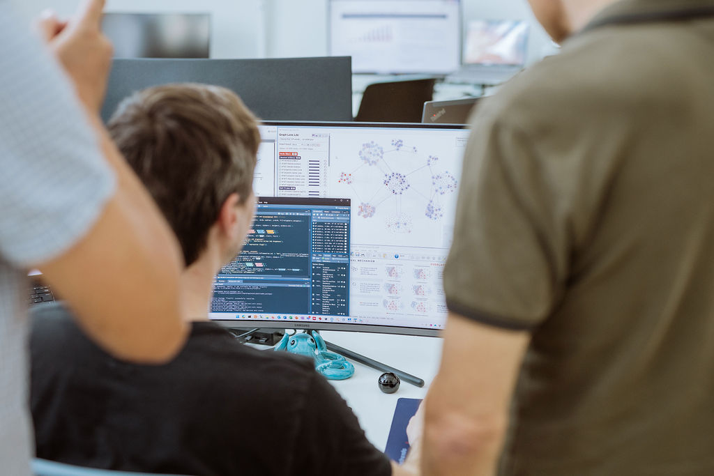 Three people look at a computer screen displaying code, graphs, and data visualizations related to personalized medicine in an office setting.