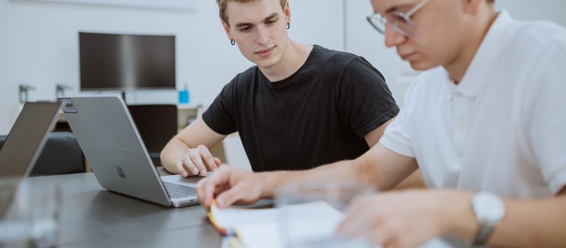 Two people sit at a table with laptops and notebooks, focused on their work in a bright, modern office setting as they collaborate on new advances in personalized medicine.