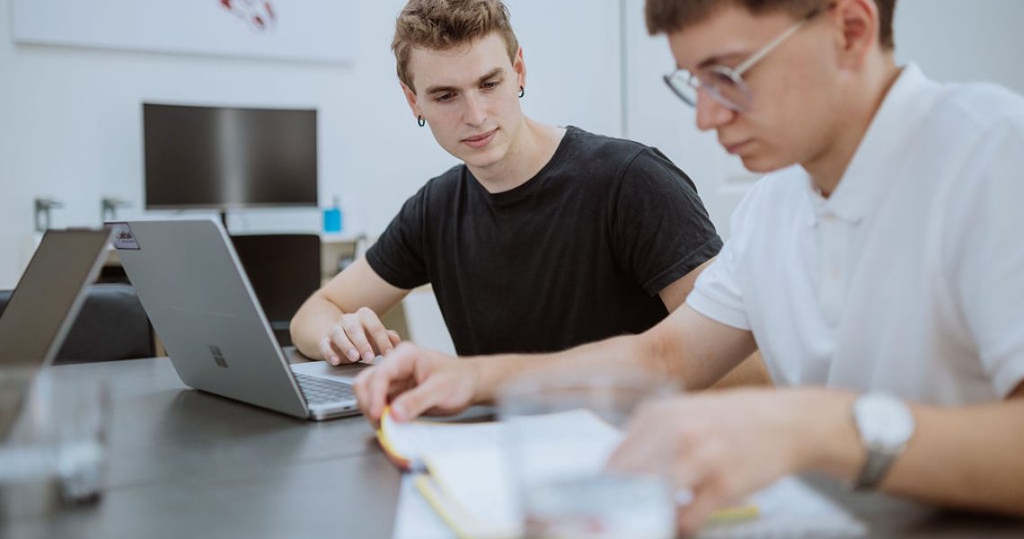 Two people sit at a table with laptops and notebooks, focused on their work in a bright, modern office setting as they collaborate on new advances in personalized medicine.