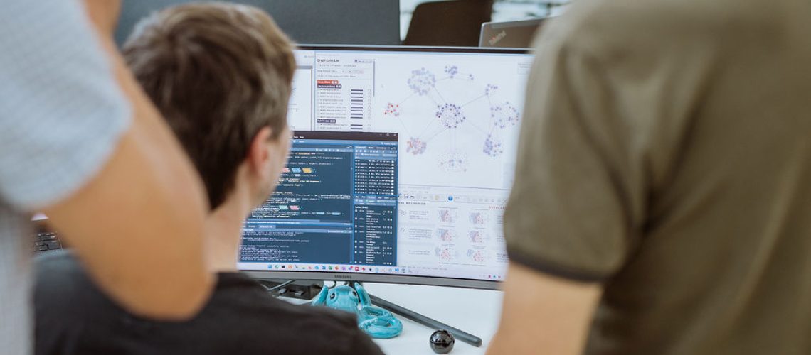 Three people look at a computer screen displaying code, graphs, and data visualizations related to personalized medicine in an office setting.