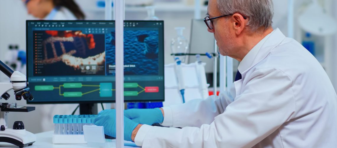 Scientist in a lab coat uses a computer displaying DNA analysis, with test tubes and a microscope nearby.